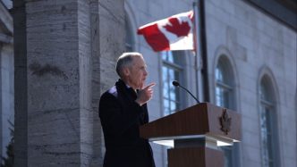 Canadian Prime Minister Mark Carney speaks at a lectern with a Canadian flag waving in the background