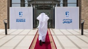 A person in traditional Emirati attire walks on a red carpet towards the entrance of the Ruwais refinery and petrochemical complex