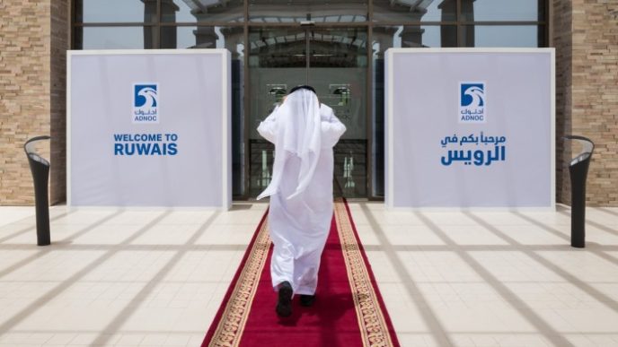 A person in traditional Emirati attire walks on a red carpet towards the entrance of the Ruwais refinery and petrochemical complex