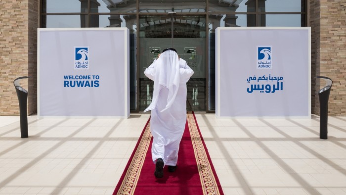 A person in traditional Emirati attire walks on a red carpet towards the entrance of the Ruwais refinery and petrochemical complex