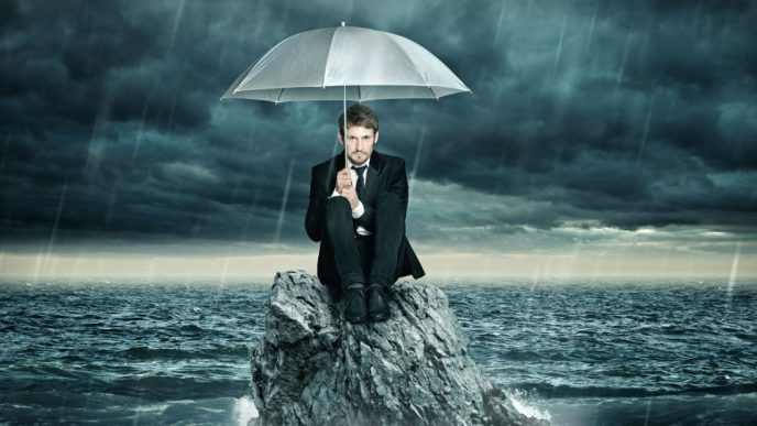 Man on rock huddled under umbrella